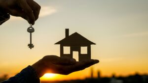 Person holding a small wooden model home and a key.